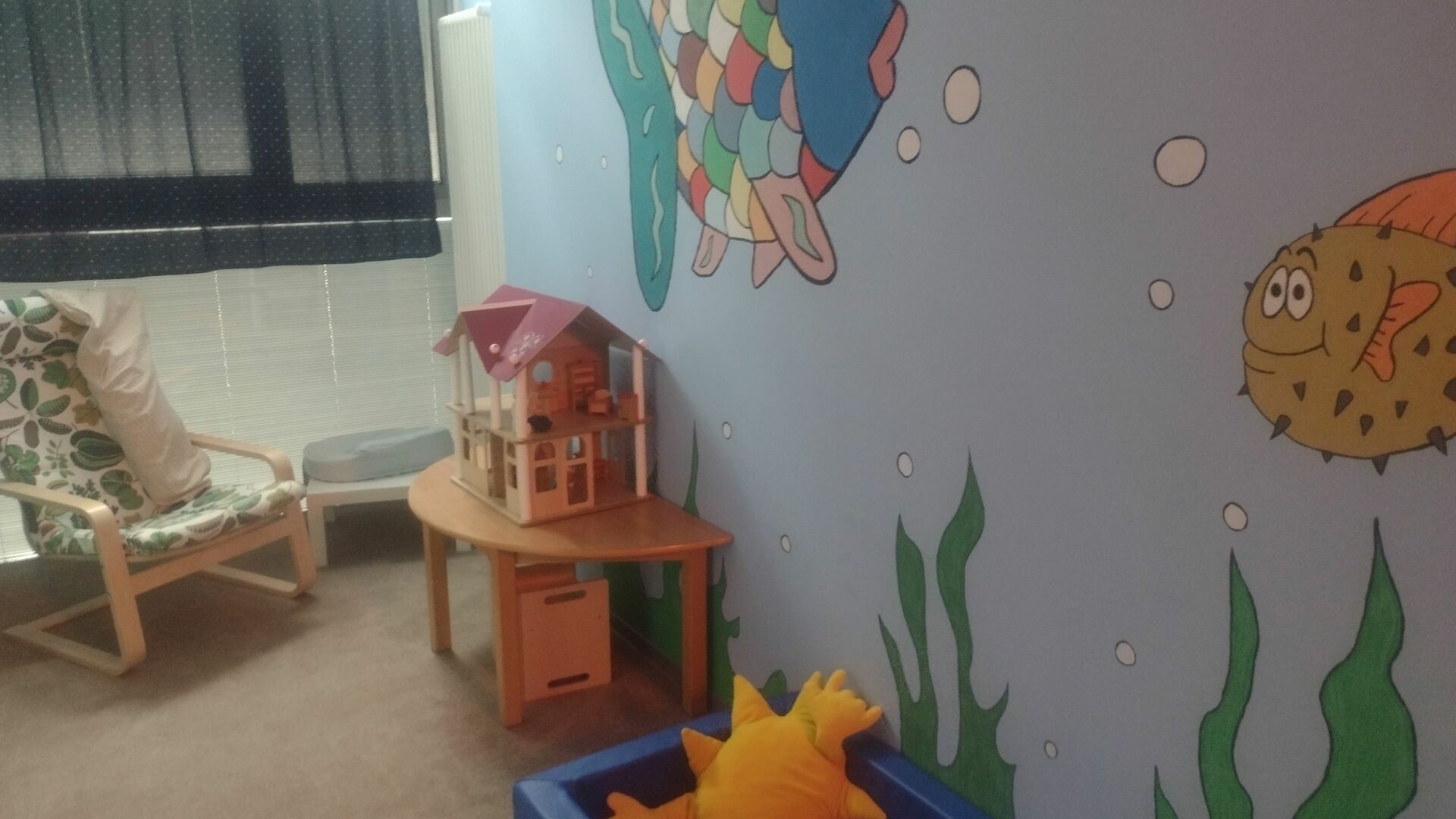 ein Kleinkindbett, ein Relaxstuhl, eine Puppenhaus und gemalte Fische an der Wand
