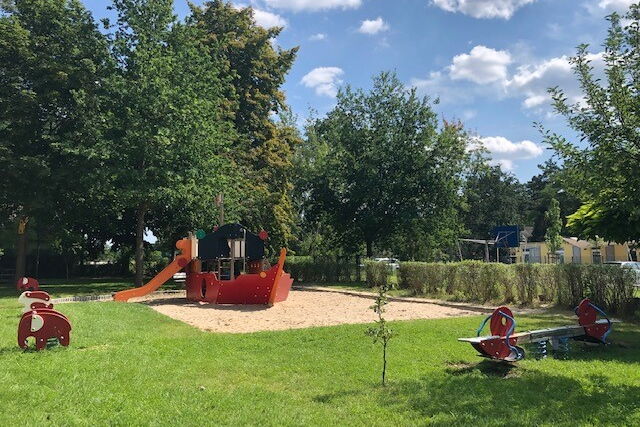 Spielplatz mit Wippe, Sandkasten und ein Klettergerüst mit Rutsche das aussieht wie ein Schiff.