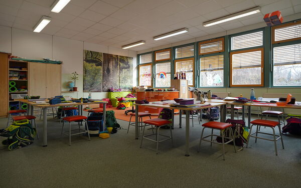 Lernzimmers. Mehrere Tische mit Hockern im Raum verteilt. Auf den Tischen liegen Federmappen und Blöcke, An den Tischen stehen Schulmappen auf dem Boden. Großer Raum.