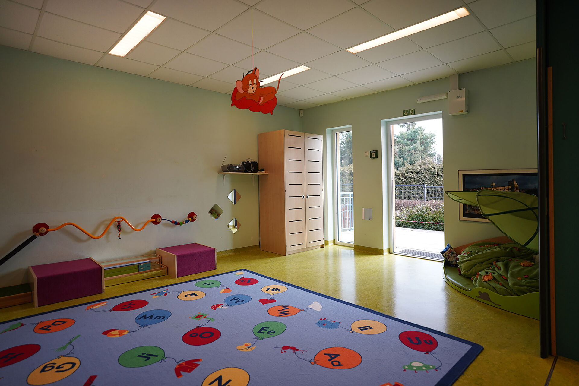 Raum mit Terrassantür. Im Raum liegt ein großer Kinderteppich mit bunten Luftballons auf denen Buchstaben stehen.