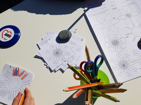 Kinder zeichnen an einem Tisch mit Buntstiften und Papier. Auf dem Tisch liegen Vorlagen für Blüten.