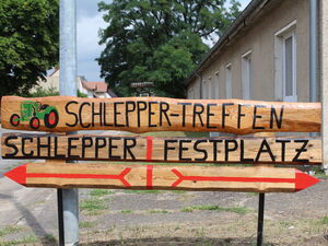 Kreatives Schild aus Holz. Darauf steht: Schleppertreffen    - Schlepper und Festplatz. Darunter 2 rote Pfeile nach links und rechts.