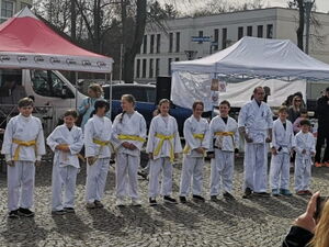 Großer Platz. Außen steh Gäste und in der Mitte eine Reihe Karateschüler in weißer Kleidung mit gelben bzw. weißen Gürtel.