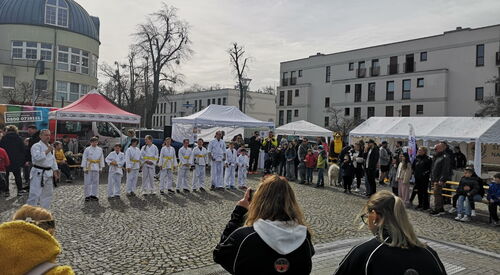 Großer Platz. Außen steh Gäste und in der Mitte eine Reihe Karateschüler in weißer Kleidung mit gelben bzw. weißen Gürtel.