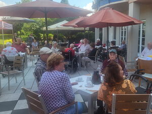 Große Terrasse mit Tischen, Stühlen und Sonnenschirmen. Mehere Personen sitzen draußen.