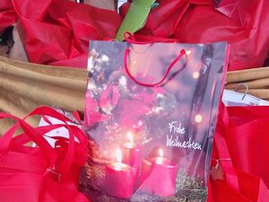 Eine Geschenktüte mit Motiv: rote Kerzen, Tannenzweige. Darauf steht: Frohe Weihnachten.