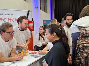 AWO Stand in einer Messehalle. 2 Männer in weißen T-Shirts mit AWWO Logo informieren eine Frau die am Stand steht.