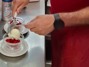 Nachtisch. Mann in roter Kleidung gibt eine Kugel Vanilleeis auf Erdbeeren in keine Glasschale.