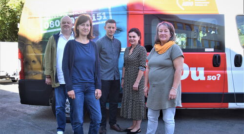 5 Personen vor einem Transporter der bunt mit mit AWO Bild bedruckt ist. 2 Männer, 3 Frauen. Die Sonne scheint.