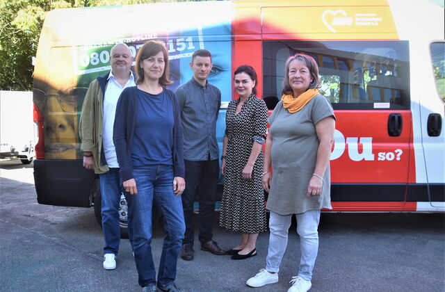 5 Personen vor einem Transporter der bunt mit mit AWO Bild bedruckt ist. 2 Männer, 3 Frauen. Die Sonne scheint.