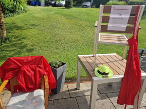 Rote Kleidung hängt über Stühlen. Auf einem Tisch liegt ein gelber Hut.