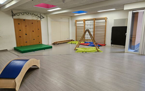 Raum mit Kletterelementen. Boulderwand, Sprossenwand und eine kleine Leiter mit schmalen Sprossen.