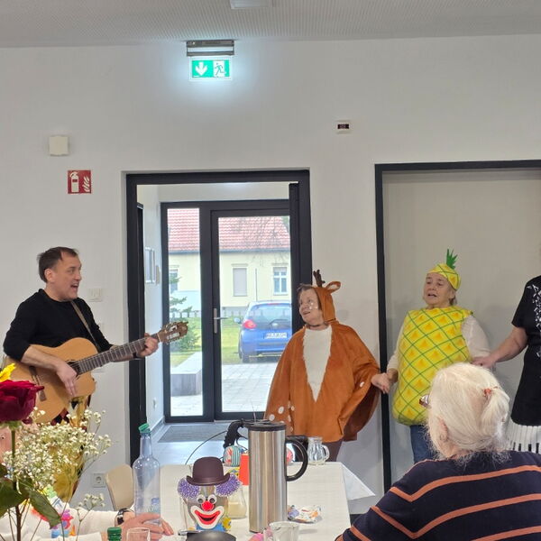 Mann mit Gitarre, zwei verkleidete Kinder und eine Frau musizieren. Kind 1 als Rehntier und Kind2 als Zitrone verkleidet.