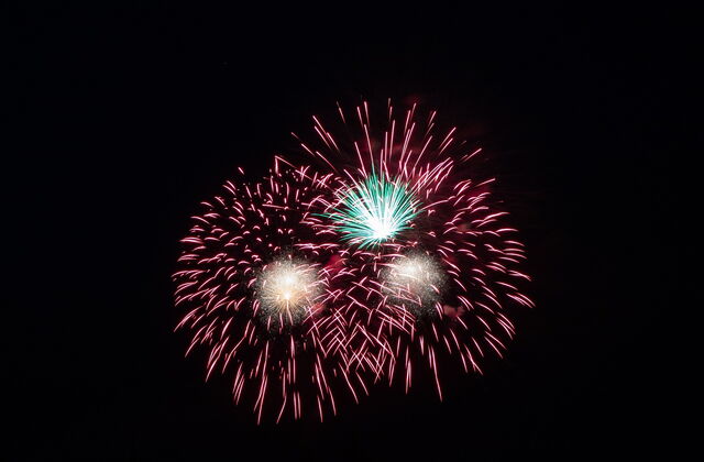 Ein Feuerwerk. Drei Feuerwerkskörper die bunt explodieren. Schwarzer Hintergrund.