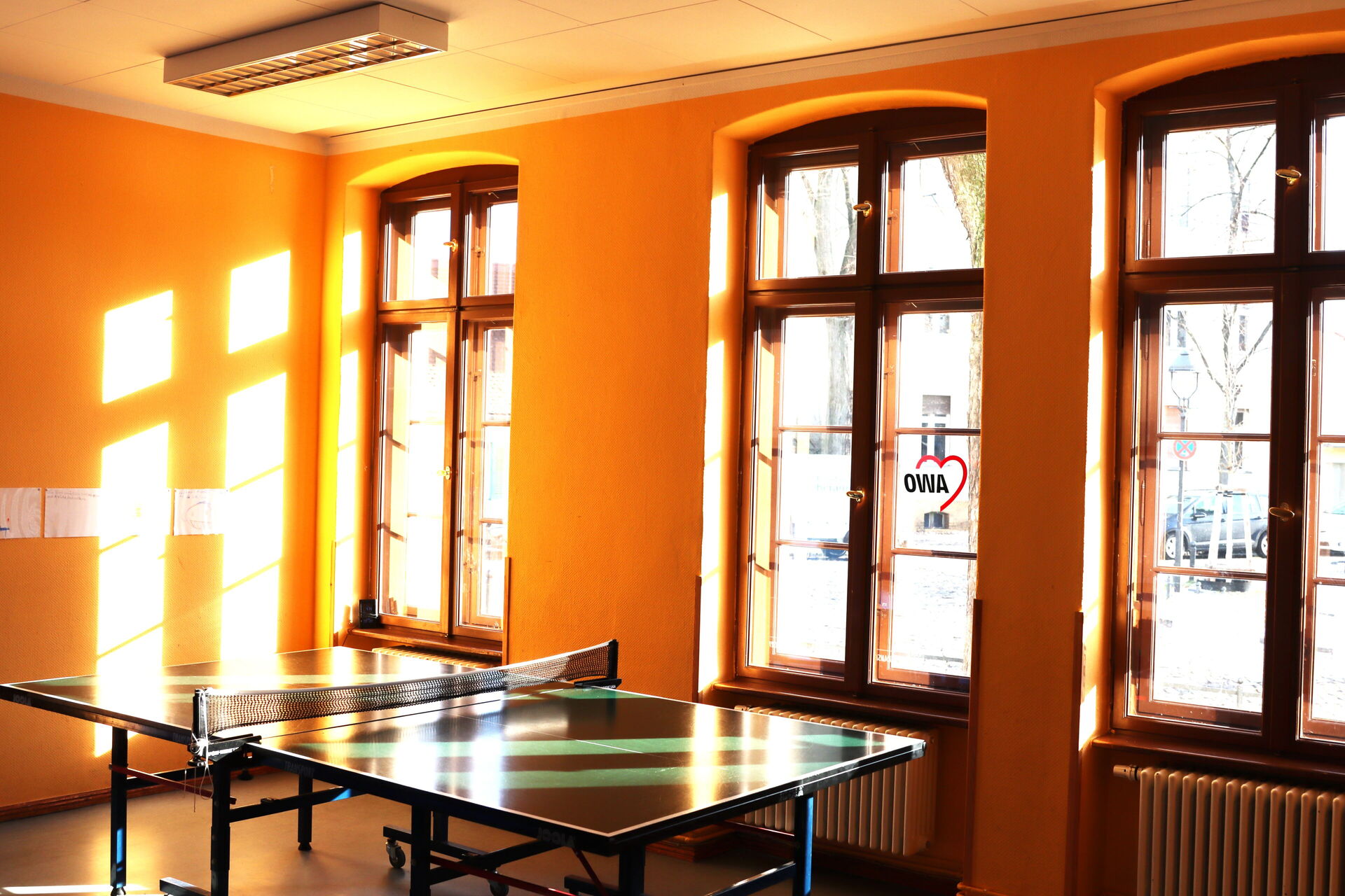 Großer Freizeitraum mit Tischtennisplatte. Große Fenster lassen viel Sonnenlicht rein.