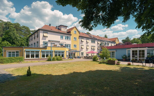 Wohnanlage. Großes Haus mit einer Terrasse davor. Wiese davor.