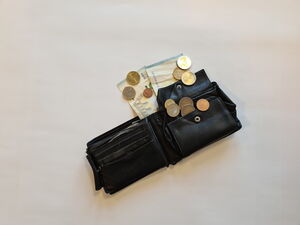 Eine geöffnete schwarze Geldbörse liegt auf einer hellen Fläche, darin und daneben liegen mehrere Euro-Münzen.