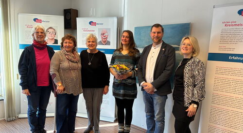 Gruppenbild vor Ausstellungstafeln. 5 Frauen und ein Mann. Die Frau in der Mitte hat einen Blumenstrauß in den Händen.