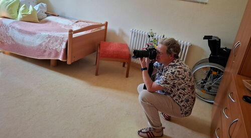 In einem Bewohnerzimmer. Eine Frau hockt mit einer Kamera und macht Fotos.