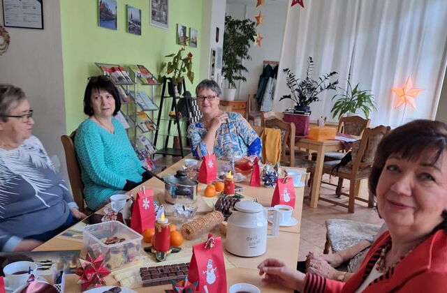 Gedeckter Kaffeetisch mit kleinen Weihnachtstüten und Süßigkeiten. Vier Frauen sitzen an dem Tisch.