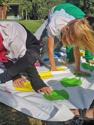 3 Kinder spielen im Freien Twister auf einer bunten Matte und stützen sich mit Händen und Füßen auf verschiedenfarbige Kreise.