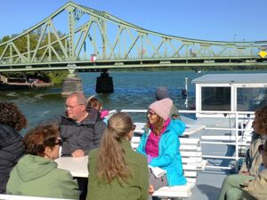 Eine Gruppe auf einem Ausflugsschiff. Das Schiff fährt in Richtung einer Brücke.