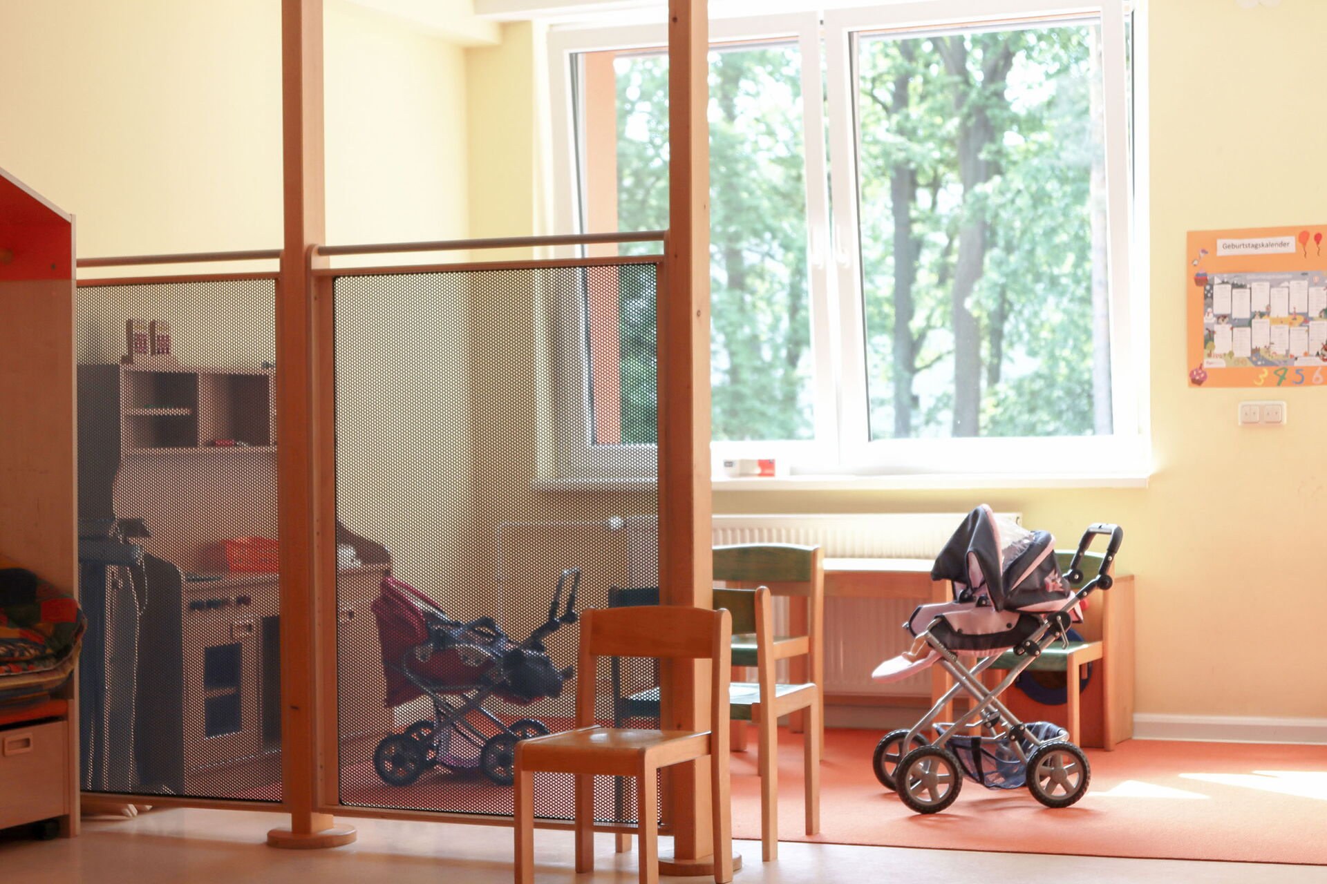 Ein Raum mit großen Fenstern. Zwei Kinderwägen stehen auf einem Teppich.