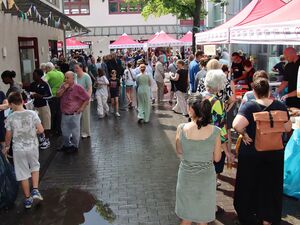 Viele Menschen auf dem Gelände. Essensstand mit roten AWO Pavillons überdacht. Gebäude rahmen das Gelände ein.