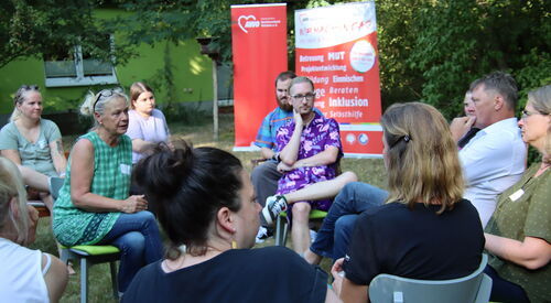 Menschen die in zwei Stuhlkreisen sitzen und miteinander ins Gespräch kommen. Im Hintergrund zwei große AWO Roll-Up Banner