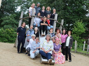 Gruppenfoto von Erwachsenen auf einem Spielplatz und Klettergerüst mit Rutsche. 20 Personen.