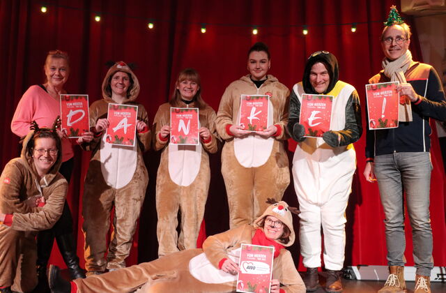 8 Personen. Viele im Rentier-Kostüm, einer als Pinguin verkleidet. Sie halten roter Schilder mit Buchstaben hoch die das Wort DANKE! bilden.