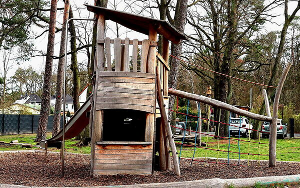 Spielplatz: Ein Holzspielturm mit einer Rutsche und einer kleinen Plattform, umgeben von Bäumen.