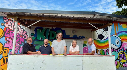 Gruppenbild. 5 Menschen, darunter eine Frau vor einer mit Graffiti besprühten Wand.