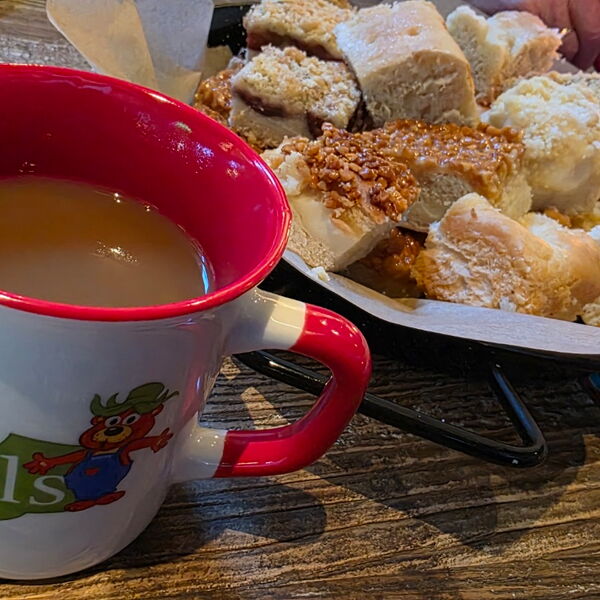Kaffee in einer Tasse vom Karls Erlebnishof und ein Teller mit Kuchenstücken.