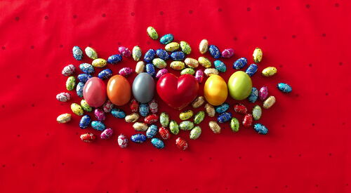 Viele bunte Ostereier liegen auf rotem Hintergrund zu einem Kreis angeordnet. In der Mitte ein rotes Herz.