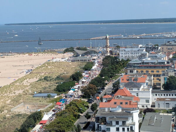 Blick von oben auf eine Küstenstadt mit Strand, Meer und Häuserreihen, vorn Geländer einer Aussichtsplattform.