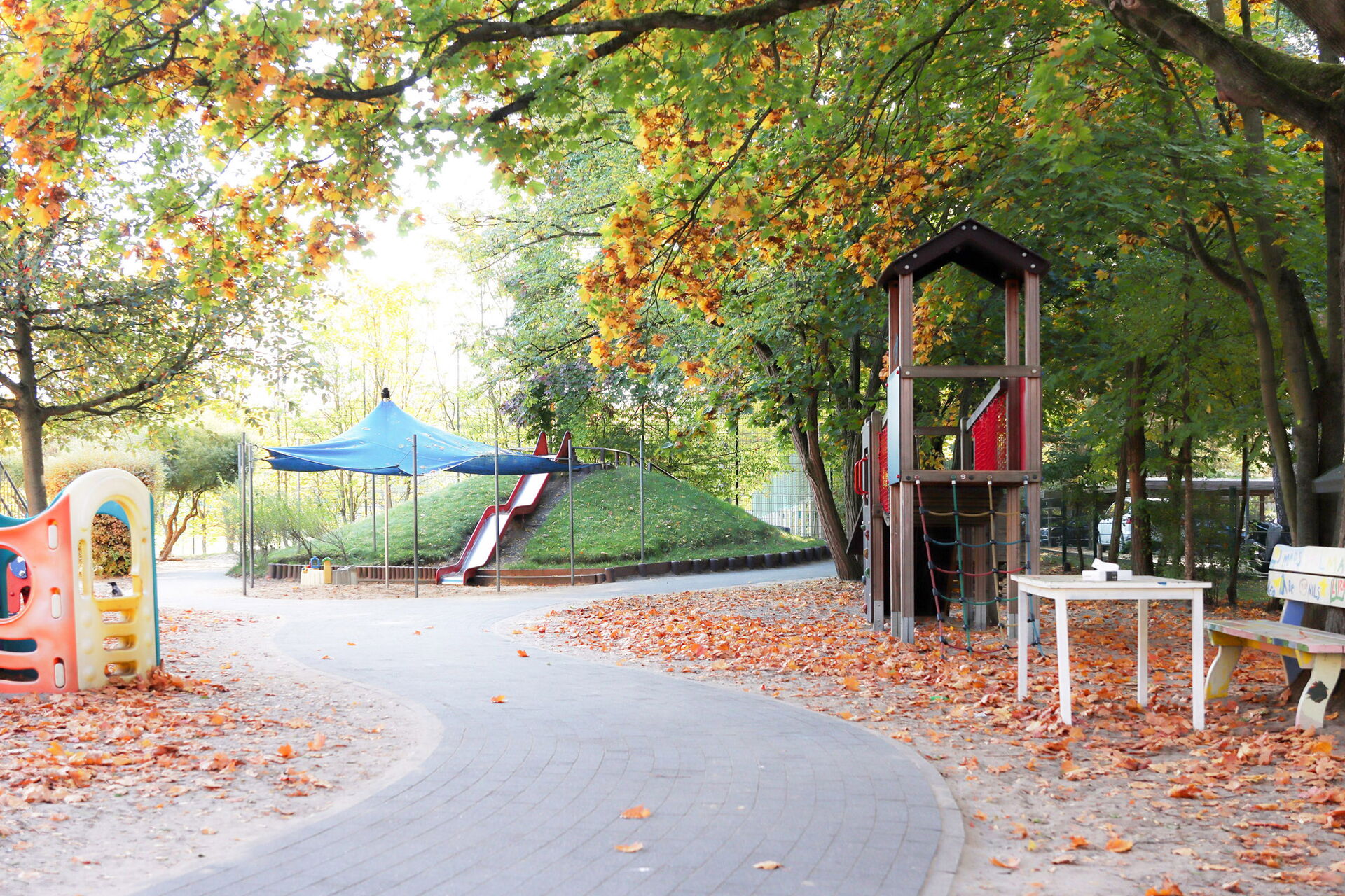 Geschlängelter Gehweg. Spielplatz, mit Klettergerüst und Rutsche. Es ist Herbst.