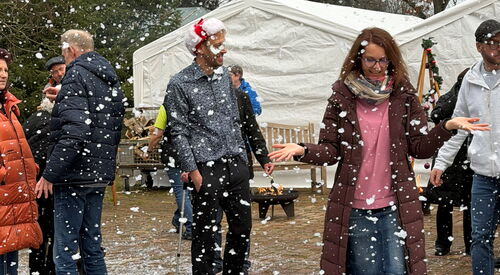 Menschen freuen sich über Kunstschneegestöber. Weiße Flocken am Boden.