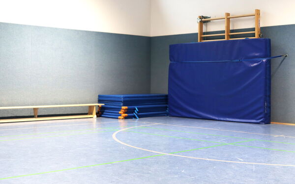 Turmhalle, an der Wand steht eine Sitzbank. Vor der Sprossenwand ist eine große blaue Weichbodenmatte gespannt.