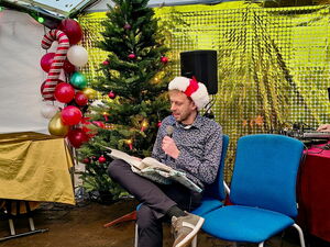 Lesung. Ein Mann mit einem großen Buch auf dem Schoß und Mikro. Die Kulisse weihnachtlich geschmückt.