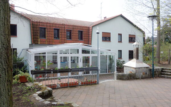 Rückansicht vom Haus mit weißer Fassade und rotem Dach. Ein Wintergarten sowie ein kleiner steinerner Kamin / Ofen für Pizza / Brot mit Schornstein.