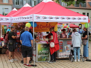 Rote AWO Pavillons: gelbes Banner: "AWO erleben"   Menschen am Stand  die sich informieren.