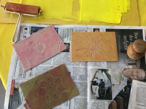3 Ton-Platten. Eine gelb mit einer eingeritzten Sonne, eine rosa mit Sonne und Blume und eine braune mit Blüte, sie liegen auf Zeitungspapier.