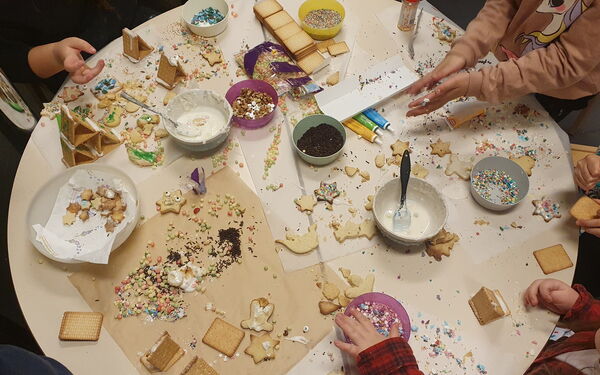 Weihnachtsplätzchen dekorieren. Runder Tisch von oben. Plätzchen, Glasuren, bunte Streusel. Kinderhände die mit dekorieren beschäftigt sind.