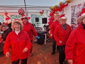 Im Festzelt. 5 Frauen die Line-Dance-Truppe. Die Frauen stehen in zwei Reihen und Tanzen. Besucher sitzen an den Tischen und essen.