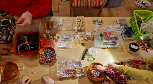 Tischplatte von oben mit vielen Schalen und Dosen mit bunten, holz Perlen. Kinder Basteln Ketten und Armbänder.