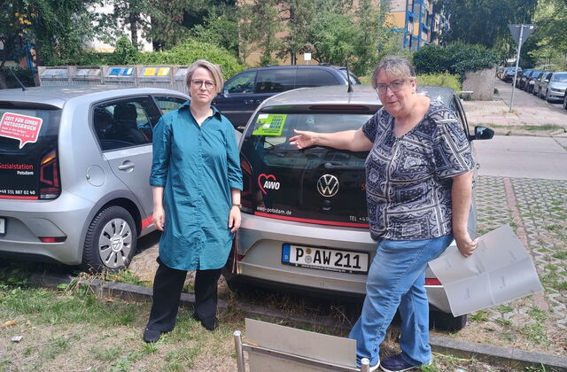 2 Frauen stehen hinter einem AWO Dienstwagen. Ein grüner Aufkleber auf der Rückscheibe: Diese Auto fährt nicht mehr, wenn...
