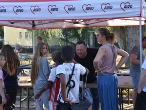 AWO Pavillon. Kinder und Erwachsene stehen davor. An dem Stand steht ein Mann der sich nach vorne beugt und mit den kindern davor spricht.