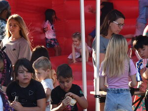 Draußen. Viele Kinder auf und vor der Hüpfburg. 4 Frauen stehen an einem Tisch mit mehreren Kindern und Jugendlichen.