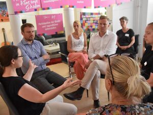 Gemütlicher Raum. 7 Menschen sitzen im Kreis und diskutieren.